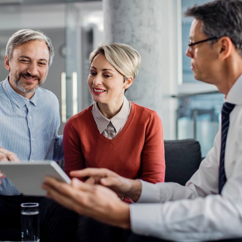 happy mid adult couple using touchpad with their financial consultant in the office